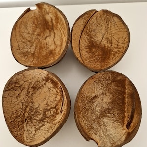 May include: Four brown coconut shell bowls, each with a unique pattern and texture. The bowls are arranged in a square shape on a white surface.