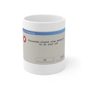 Może przedstawiać: Biały ceramiczny kubek z grafiką przedstawiającą komunikat o błędzie komputera. Projekt zawiera niebieski pasek tytułowy, czerwone kółko z białym znakiem X oraz tekst: "Alexander, please stop asking ai to do your job" z przyciskami OK i Cancel.
