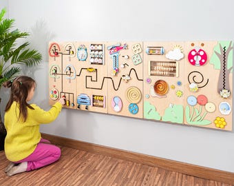 May include: A large wooden activity board with various interactive elements for children. Features include a clock, abacus, gears, and a car. The board is mounted on a wall, with a child interacting with it.