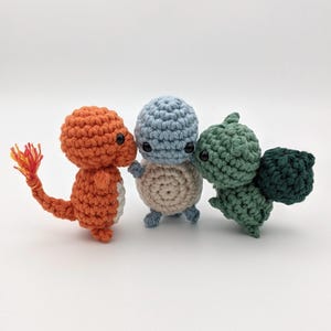 May include: Three crocheted stuffed toys, a red and orange one with a tail, a blue and beige one, and a green one with a tail. The toys are all facing each other.