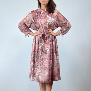 May include: A vintage floral print dress in shades of pink, white, and black. The dress features long sleeves with tie details at the cuffs, a button-up front, and a matching tie belt. The dress falls to mid-calf length.