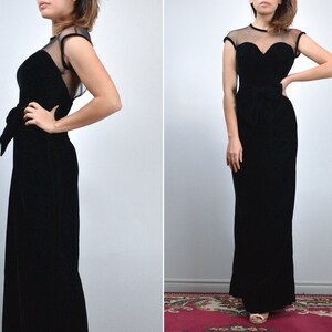 May include: A black velvet evening gown with a sweetheart neckline and sheer cap sleeves. The dress features a fitted bodice, a bow at the waist, and a floor-length skirt. The gown is a classic, elegant design.