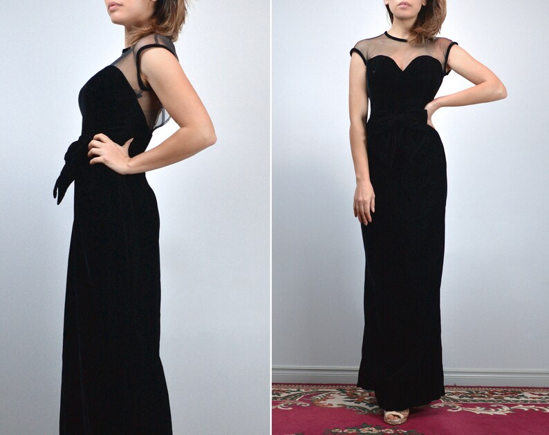 May include: A black velvet evening gown with a sweetheart neckline and sheer cap sleeves. The dress features a fitted bodice, a bow at the waist, and a floor-length skirt. The gown is a classic, elegant design.