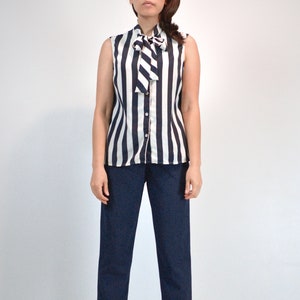 May include: A sleeveless blouse with a black and white striped pattern and a white bow tie at the neck.