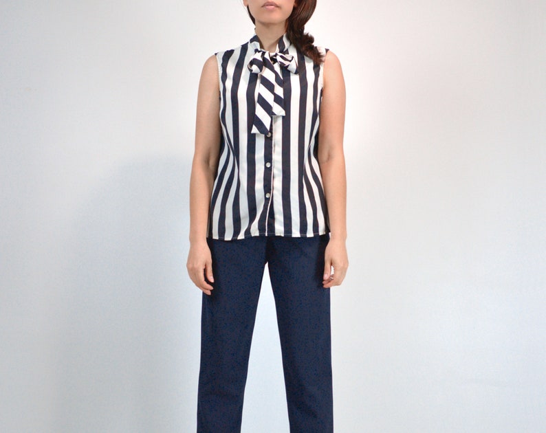 May include: A sleeveless blouse with a black and white striped pattern and a white bow tie at the neck.