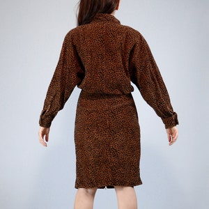 Pu&ograve; includere: Un abito marrone e nero con stampa leopardata, con maniche lunghe e collo a camicia. L'abito ha una vita aderente e una gonna al ginocchio. Il tessuto sembra essere un materiale morbido e strutturato.