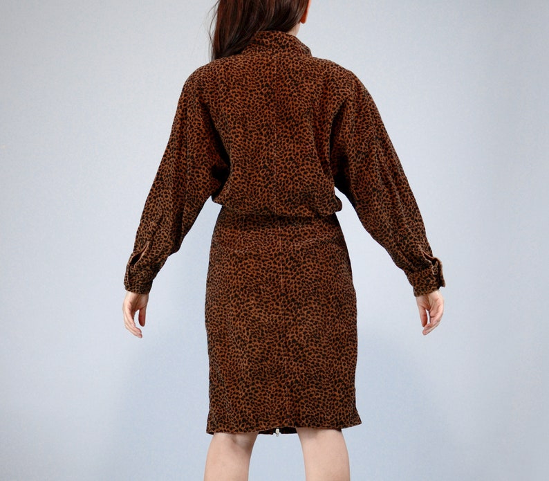 Pu&ograve; includere: Un abito marrone e nero con stampa leopardata, con maniche lunghe e collo a camicia. L'abito ha una vita aderente e una gonna al ginocchio. Il tessuto sembra essere un materiale morbido e strutturato.