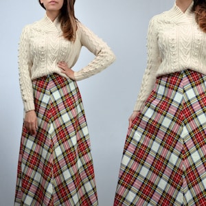 Puede incluir: Un su&eacute;ter de punto trenzado color crema con cuello alto y una falda larga a cuadros en rojo, blanco, amarillo y negro. La falda tiene forma de l&iacute;nea A. El conjunto es de estilo vintage.