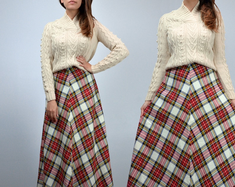 Puede incluir: Un su&eacute;ter de punto trenzado color crema con cuello alto y una falda larga a cuadros en rojo, blanco, amarillo y negro. La falda tiene forma de l&iacute;nea A. El conjunto es de estilo vintage.