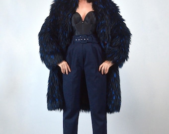 May include: A long, shaggy faux fur coat in black with vibrant blue highlights, worn over a black structured corset top and high-waisted navy blue trousers featuring a matching fabric belt with a rectangular buckle at the waist.