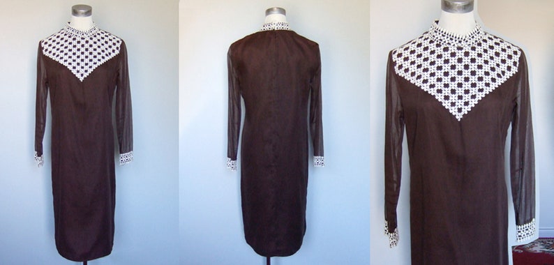May include: A brown dress with a white, geometric patterned collar and cuffs. The dress has long, sheer sleeves and a straight silhouette. The dress is displayed on a mannequin, showcasing its vintage style and design.