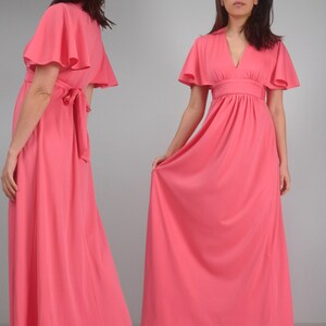 May include: A coral maxi dress with short, flared sleeves and a V-neck. The dress has a fitted waist and a flowing skirt. The back view shows a tie detail at the waist. The dress is made of a soft, flowing fabric.