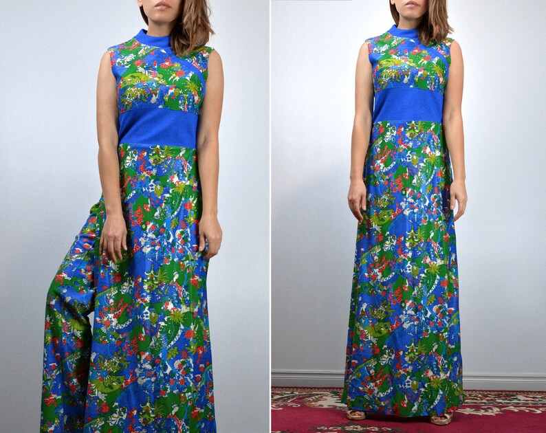 May include: A long, sleeveless dress with a colourful floral print in blue, green, and red. The dress has a high neckline and a solid blue band at the waist. The fabric looks lightweight, ideal for warmer weather. The dress is floor-length.