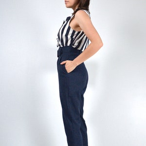 May include: A woman wearing a striped sleeveless blouse and dark blue high-waisted pants with a belt.