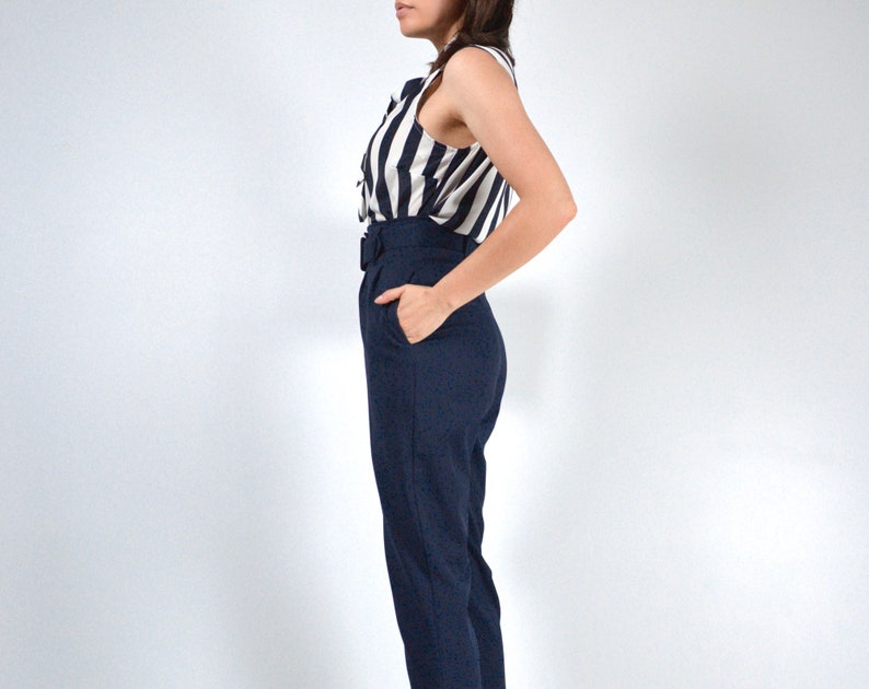 May include: A woman wearing a striped sleeveless blouse and dark blue high-waisted pants with a belt.