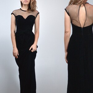 May include: A black velvet evening gown with a sheer neckline and cap sleeves. The bodice features a sweetheart neckline and a fitted waist. The back of the dress has a sheer panel. The dress is floor-length.