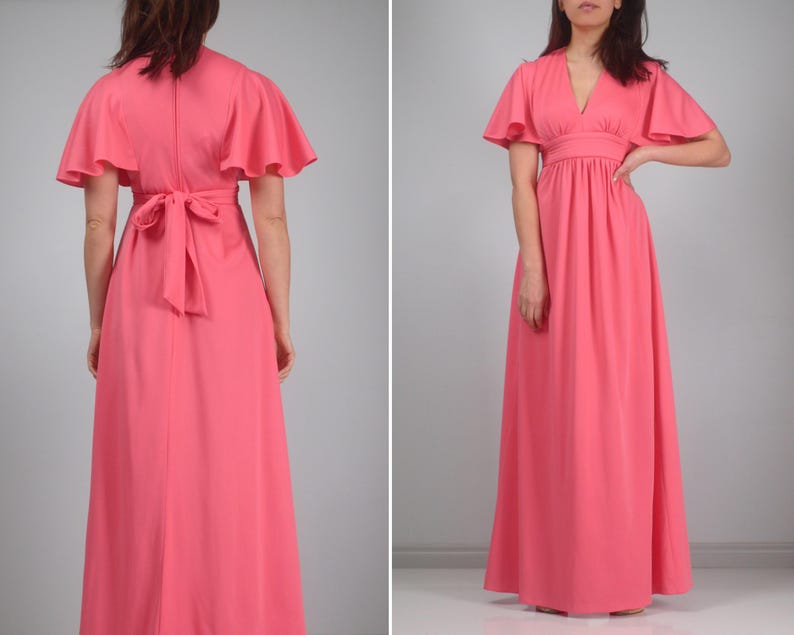 May include: A coral maxi dress with short, flared sleeves and a V-neck. The dress has a fitted waist and a flowing skirt. The back of the dress features a tie detail at the waist. The dress is made of a smooth, solid fabric.