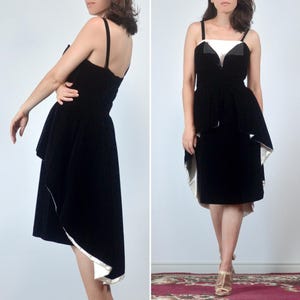 May include: A black velvet dress featuring a white bodice insert, thin shoulder straps, and a high-low hemline with a white lining. The garment has a fitted waist and a layered skirt design that is shorter in the front and longer in the back.