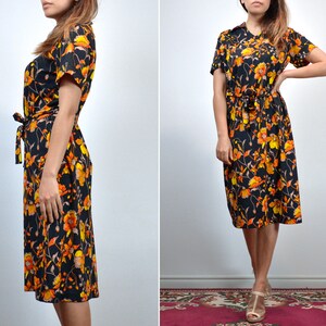 Puede incluir: Un vestido midi negro con estampado floral en naranja y amarillo. El vestido tiene un lazo en la cintura y mangas cortas.