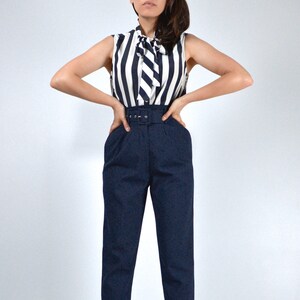 May include: A woman wearing a navy blue and white striped sleeveless blouse with a bow tie and a pair of high-waisted navy blue pants with a belt.