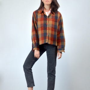 May include: A long-sleeved plaid shirt in shades of orange, brown, blue, and black. The shirt has a button-up front and a relaxed fit.