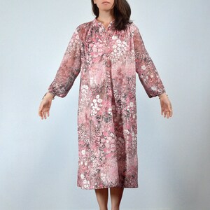 May include: A vintage floral print dress in shades of pink, white, and gray. The dress features long sleeves, a mandarin collar, and a button-down front. The fabric appears to be sheer, with a delicate, flowing silhouette.