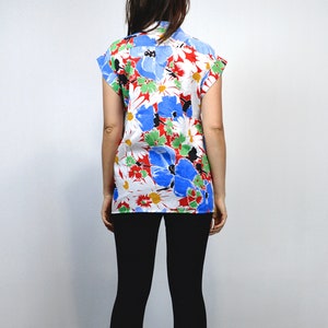 May include: A short-sleeved shirt with a vibrant floral pattern. The shirt features large blue, red, and white flowers with green leaves against a white background. The shirt is worn with black leggings.