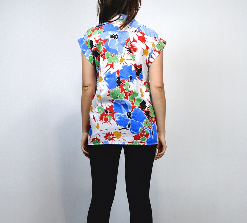 May include: A short-sleeved shirt with a vibrant floral pattern. The shirt features large blue, red, and white flowers with green leaves against a white background. The shirt is worn with black leggings.