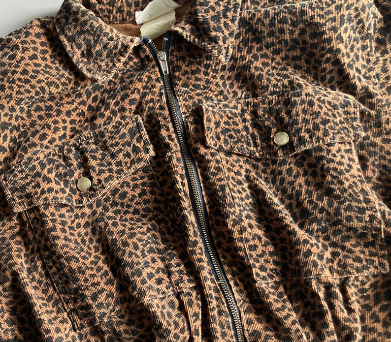 Pu&ograve; includere: Giacca marrone e nera con stampa leopardata, chiusura con cerniera, due tasche sul petto con bottoni e colletto. La giacca &egrave; in tessuto di velluto a coste.