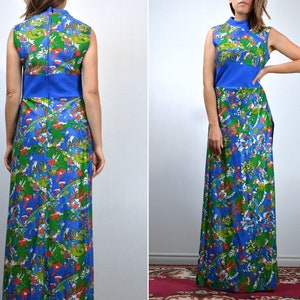 May include: A sleeveless maxi dress with a high neckline. The dress has a blue bodice and a vibrant print of green, red, and white floral and abstract shapes on a blue background. The dress has a fitted waist and a long, flowing skirt.