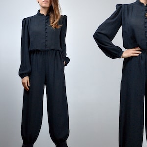 May include: A black long-sleeved jumpsuit with a high neckline and button closure. The jumpsuit has a relaxed fit and features a wide leg.
