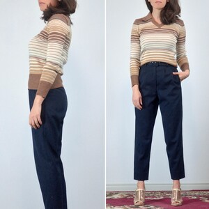 May include: A vintage outfit featuring a brown, tan, and cream striped long-sleeve sweater with a collared neckline. Paired with high-waisted, navy blue trousers. The outfit is completed with gold-colored heels.
