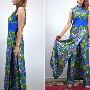 May include: A vintage jumpsuit with a sleeveless design, featuring a colourful floral pattern in blue, green, and red. It has a high neckline, a solid blue band at the waist, and a split-leg style. The fabric has a silky sheen.