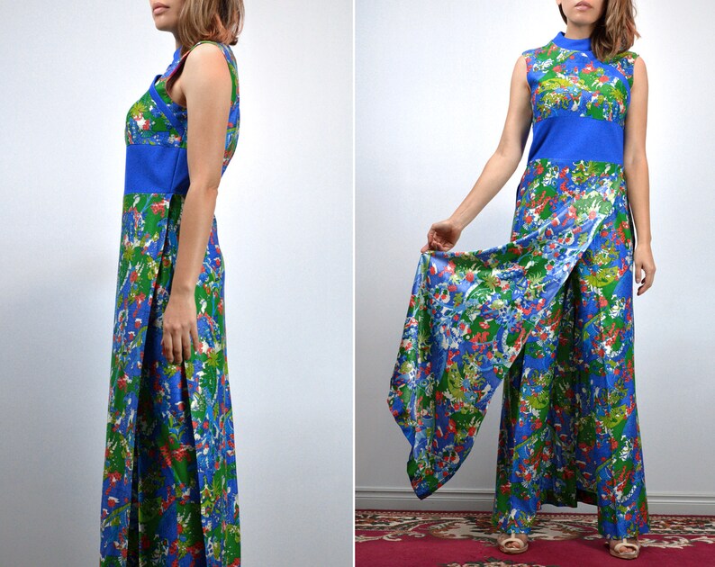 May include: A vintage jumpsuit with a sleeveless design, featuring a colourful floral pattern in blue, green, and red. It has a high neckline, a solid blue band at the waist, and a split-leg style. The fabric has a silky sheen.
