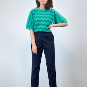 May include: A teal and green chevron-patterned jumper with short sleeves and navy blue trousers. The jumper has a fuzzy texture and a crew neck. The trousers are straight-legged and have a classic design. The outfit is suitable for casual wear.