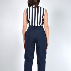 May include: A woman wearing a black and white striped sleeveless top and dark blue high-waisted pants.