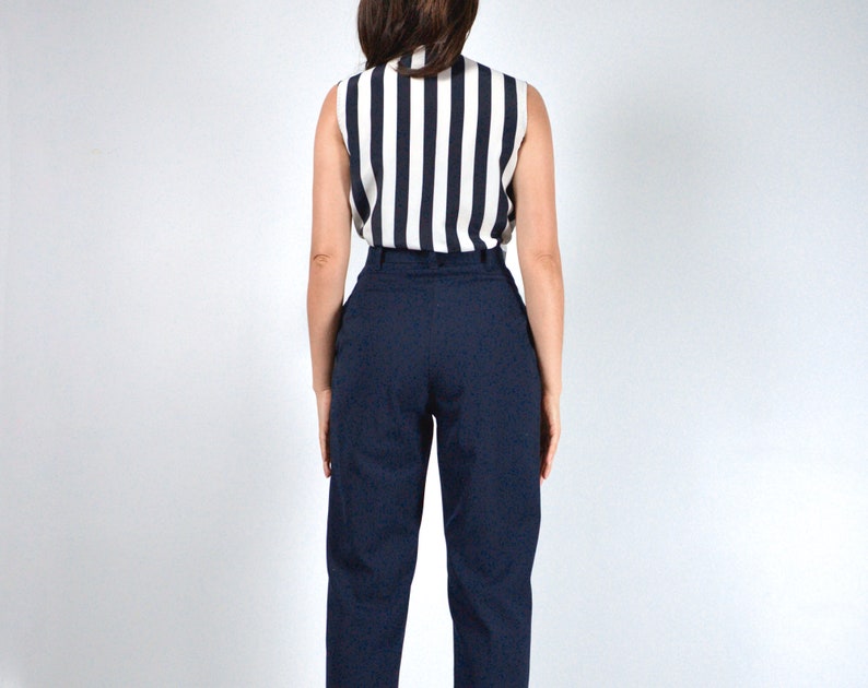 May include: A woman wearing a black and white striped sleeveless top and dark blue high-waisted pants.