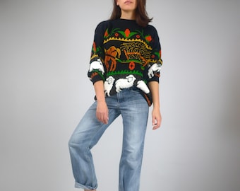 May include: A black sweater with a colorful design featuring sheep, a horse-drawn carriage, and floral accents. The sweater is paired with light blue denim jeans.