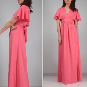 May include: A coral maxi dress with short, flared sleeves and a V-neck. The dress has a cinched waist and a flowing skirt. A matching sash is tied at the back. The dress is made of a lightweight fabric.