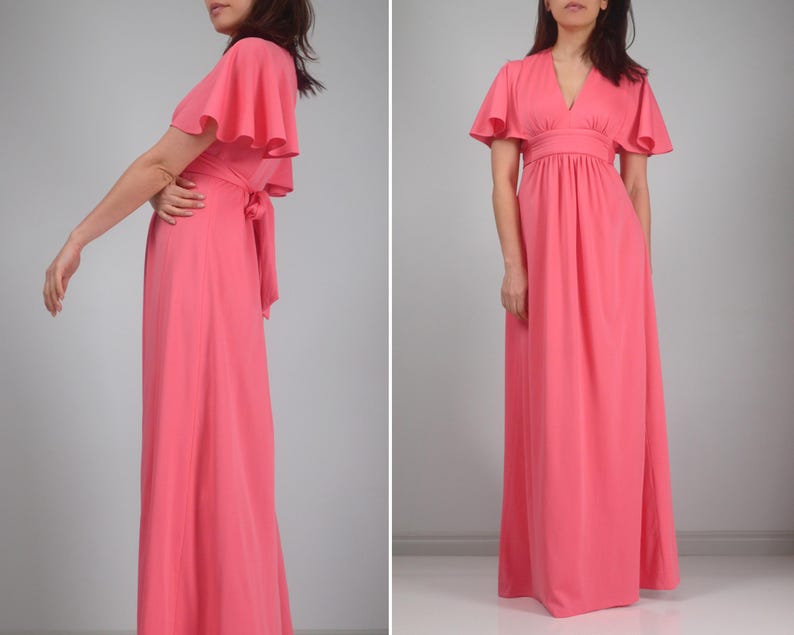 May include: A coral maxi dress with short, flared sleeves and a V-neck. The dress has a cinched waist and a flowing skirt. A matching sash is tied at the back. The dress is made of a lightweight fabric.