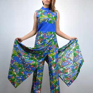 May include: A sleeveless jumpsuit in a vibrant blue, green, and red floral pattern. The jumpsuit features a high neckline, a blue waist panel, and wide-leg trousers with attached fabric panels that extend outward. The fabric has a vintage aesthetic.