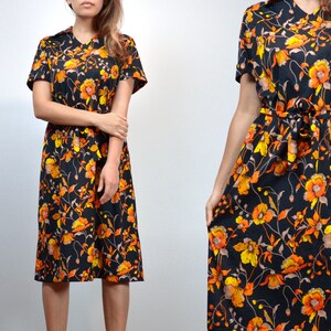 Puede incluir: Un vestido midi negro con estampado floral con flores naranjas y amarillas. El vestido tiene manga corta y un lazo en la cintura.