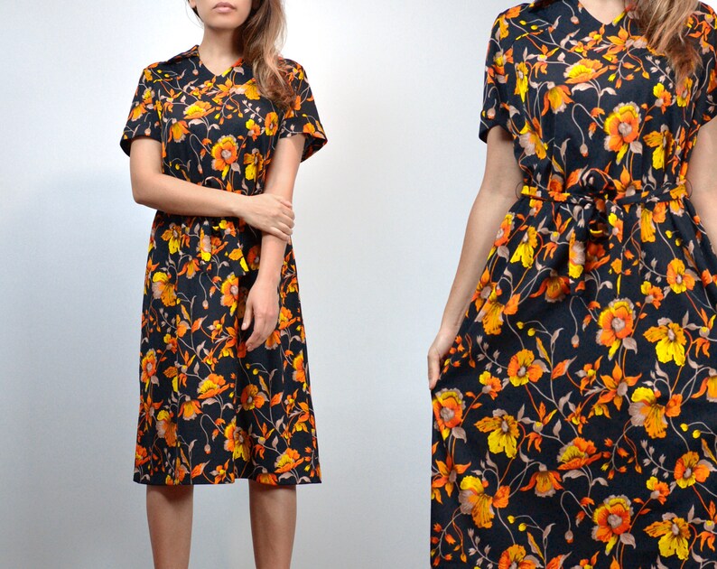 Puede incluir: Un vestido midi negro con estampado floral con flores naranjas y amarillas. El vestido tiene manga corta y un lazo en la cintura.