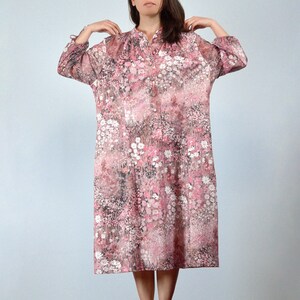 May include: A knee-length, button-down dress with a floral pattern in shades of pink, white, and brown. The dress has long sleeves and a mandarin collar. The fabric appears to be lightweight and semi-sheer.