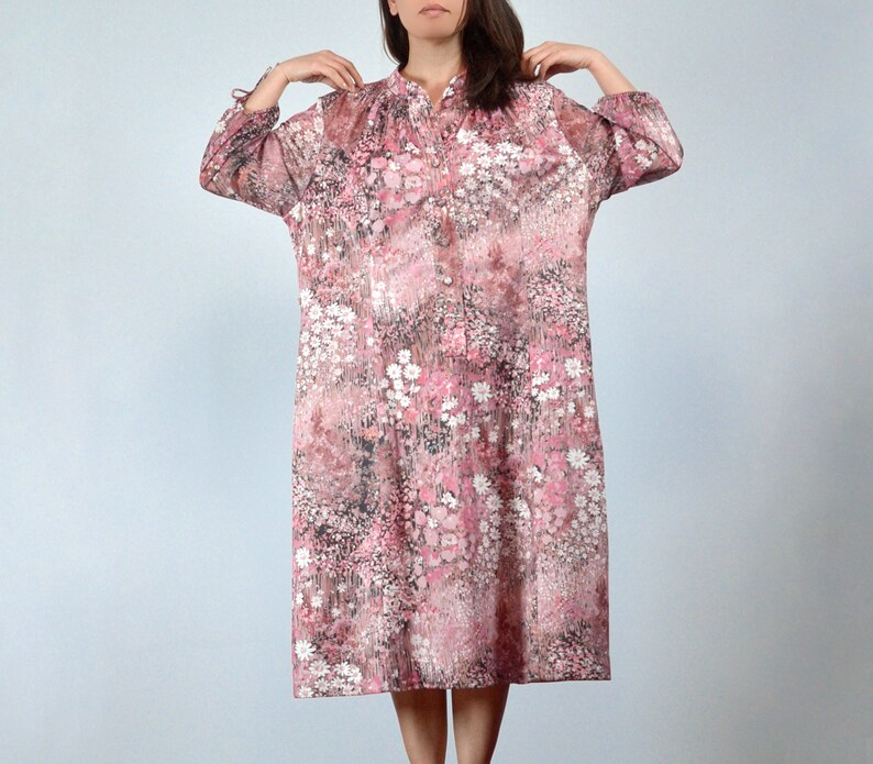 May include: A knee-length, button-down dress with a floral pattern in shades of pink, white, and brown. The dress has long sleeves and a mandarin collar. The fabric appears to be lightweight and semi-sheer.