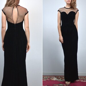 May include: A black evening gown with a sheer neckline and cap sleeves. The dress features a sweetheart bodice and a floor-length skirt. The back of the dress has a keyhole design. The gown is made of a velvet-like material.