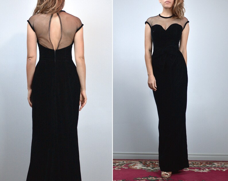 May include: A black evening gown with a sheer neckline and cap sleeves. The dress features a sweetheart bodice and a floor-length skirt. The back of the dress has a keyhole design. The gown is made of a velvet-like material.