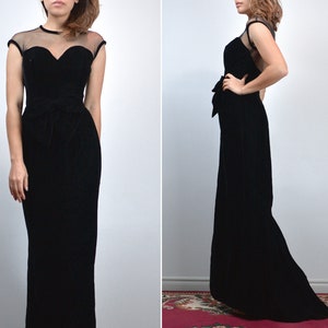 May include: A black velvet evening gown with a sweetheart neckline and sheer cap sleeves. The dress features a fitted bodice, a cinched waist with a bow detail, and a floor-length skirt. The gown is a classic, elegant design.