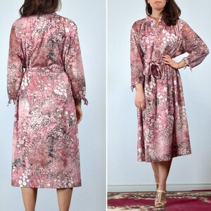 May include: A vintage midi dress featuring a floral pattern in shades of pink, white, and black. The dress has long sleeves with tie details at the cuffs, a tie waist, and a collared neckline. The dress is knee-length.