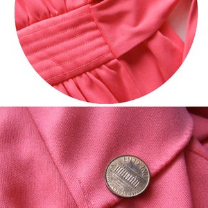 May include: Close-up of a coral-coloured garment, possibly a dress or top, with detailed stitching and a bow. A penny is placed on the fabric for scale, highlighting the texture and colour.